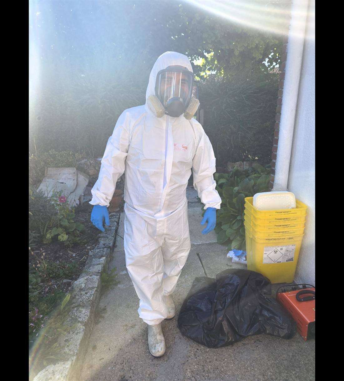 Intervenant Nettoyage Après Décès 94 en combinaison et masque, avec bacs DASRI, lors d'une décontamination dans le Val-de-Marne
